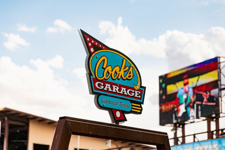 The colorful retro Cook's Garage sign in Lubbock, Texas, with a live music stage visible in the background.