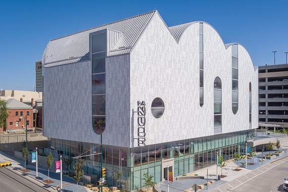 The exterior of La Nube STEAM Discovery Center in downtown El Paso, a four-story building with a scalloped cloud-like roofline, pale patterned cladding, and arched windows above a glass ground floor.