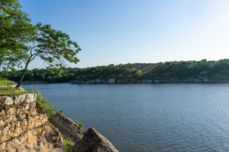 Limestone bluffs and calm open water on Lake Texoma near Denison, Texas, with lush green trees along the shoreline on a clear summer day.
