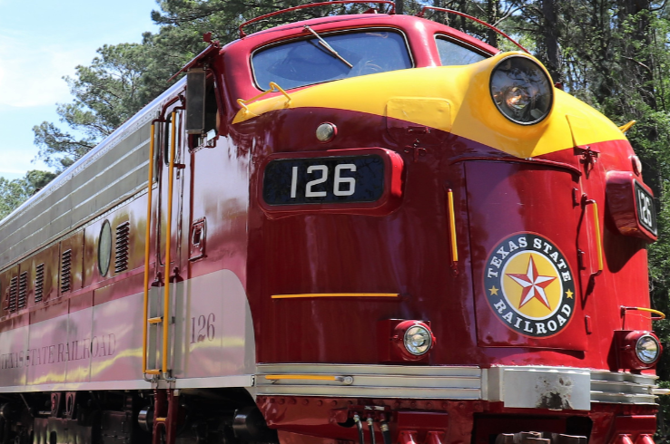 A vintage red and yellow Texas State Railroad locomotive numbered 126 sits on the tracks in Palestine, TX.