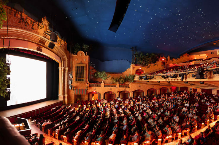Inside the Plaza Theatre in El Paso, Texas — a 1930 Spanish Colonial Revival movie palace — a packed audience watches a film beneath the atmospheric starlit ceiling, with ornate balconies, arched facades, and period architecture surrounding the illuminated screen.