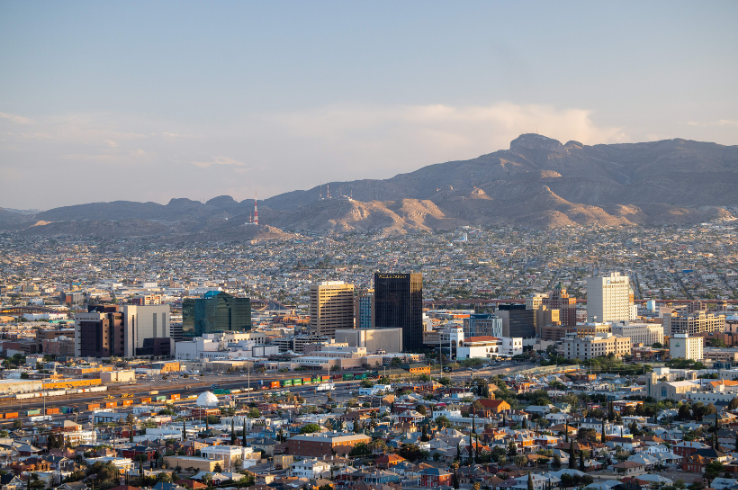 The view from Scenic Drive Overlook in El Paso, looking across downtown high-rises and low residential rooftops toward the Franklin Mountains and the Sierra de Juárez beyond.