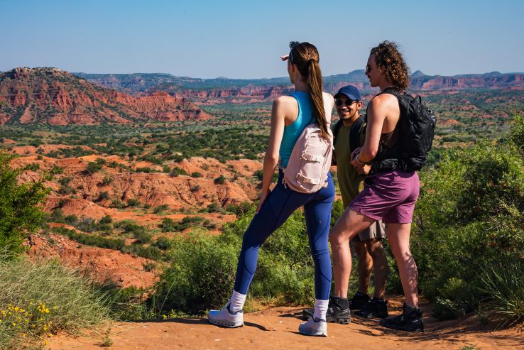 Three hikers with backpacks take in the red rock vistas of Caprock Canyons State Park.