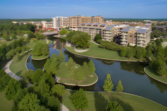 A scenic park in Addison features a tree-lined walking path, open green space, and landscaped gardens under a bright blue Texas sky.